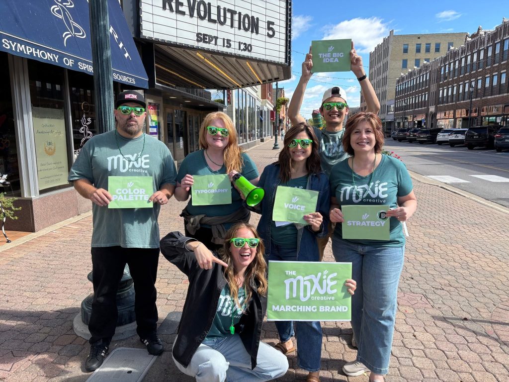 The Moxie Creative team in matching Moxie shirts holding signs downtown